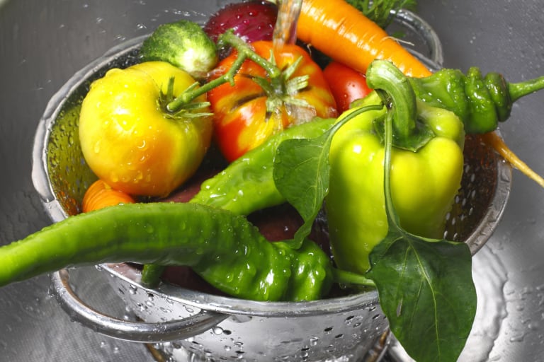 Vegetables in colander under running water.